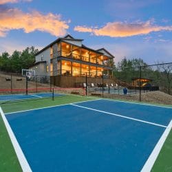 Blue and green pickleball-style court with a basketball goal, and the lodge behind it at dusk