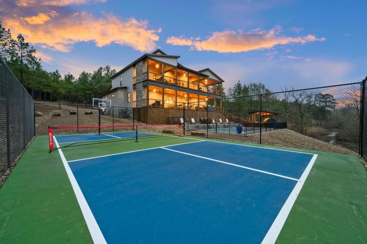 Blue and green pickleball-style court with a basketball goal, and the lodge behind it at dusk