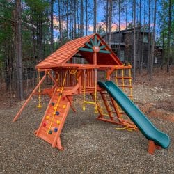 Wooden playset with a green slide and climbing wall in the pines