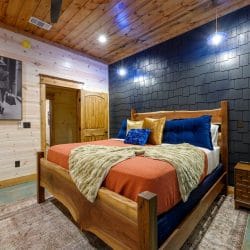 King bed with orange cover and navy pillows against a dark shingle wall