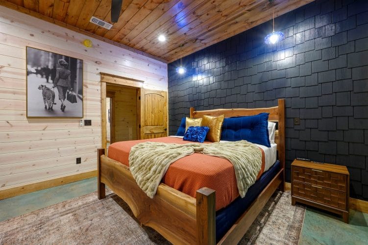 King bed with orange cover and navy pillows against a dark shingle wall
