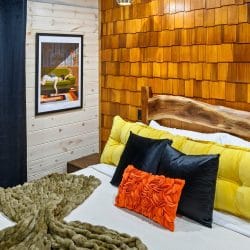 Close view of a yellow headboard and orange pillow on a bed against a shingle wall