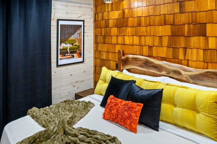 Close view of a yellow headboard and orange pillow on a bed against a shingle wall