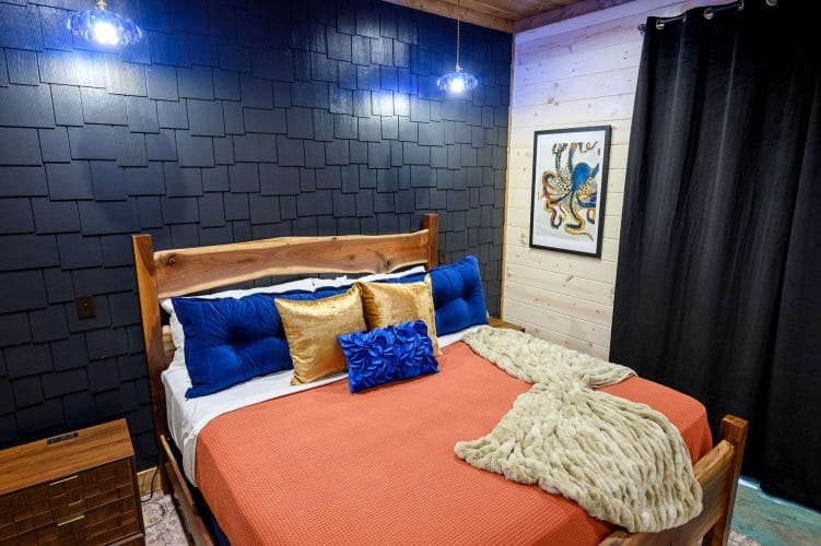 King bed with coral cover and blue and gold pillows against a navy shingle wall