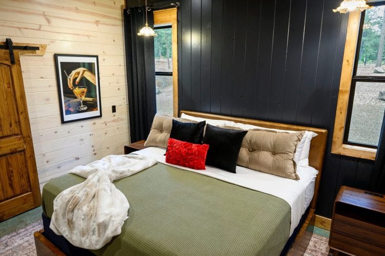King bed with olive cover, black and red pillows and a dark wall