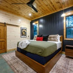 King bed with olive cover, dark wall and a barn door
