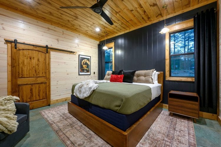 King bed with olive cover, dark wall and a barn door