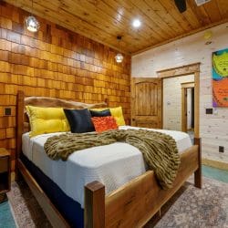 King bed with white bedding and yellow pillows against a wood-shingle wall