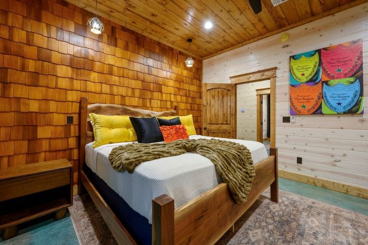 King bed with white bedding and yellow pillows against a wood-shingle wall