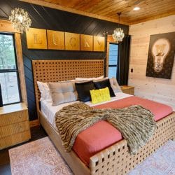 King bed with coral cover and a woven wood headboard under a lit chandelier