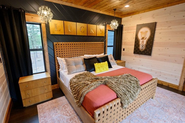 King bed with coral cover and a woven wood headboard under a lit chandelier