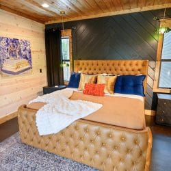 King bed with a tufted tan headboard, orange and blue pillows and a white throw