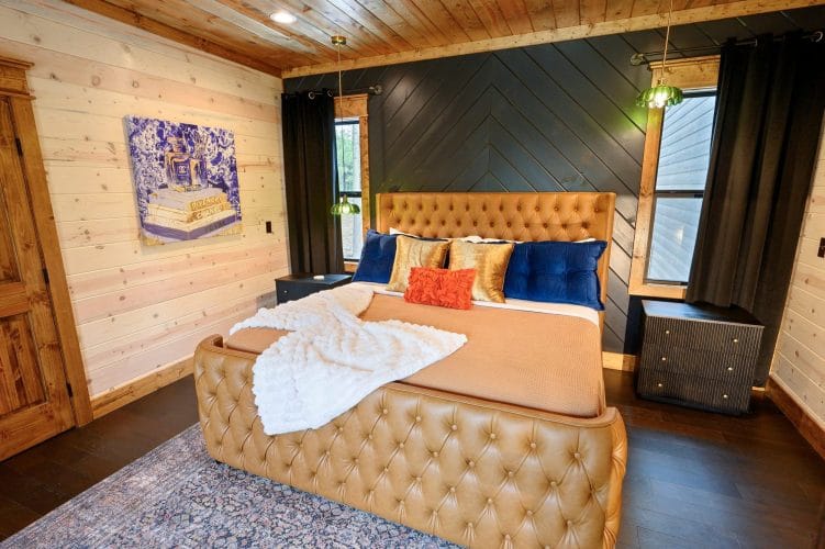 King bed with a tufted tan headboard, orange and blue pillows and a white throw