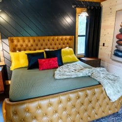 King bed with a tufted leather headboard, green cover and yellow pillows