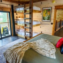 King bed with green cover and a bunk stack behind, sliding door to a balcony