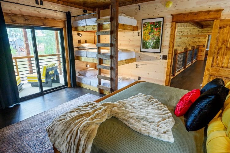 King bed with green cover and a bunk stack behind, sliding door to a balcony