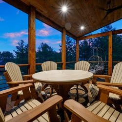 Round table with chairs and a hanging egg chair on a covered deck at dusk