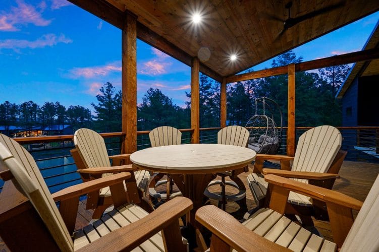 Round table with chairs and a hanging egg chair on a covered deck at dusk