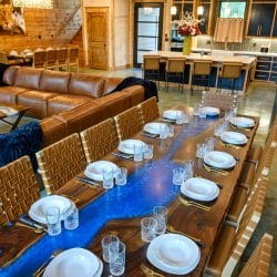 Long wood-and-blue-resin dining table set for a big meal, leather sectional beyond