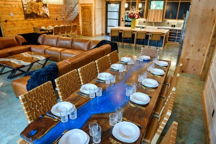 Long wood-and-blue-resin dining table set for a big meal, leather sectional beyond