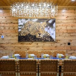 Long dining table under a chandelier with a leopard painting on the wall