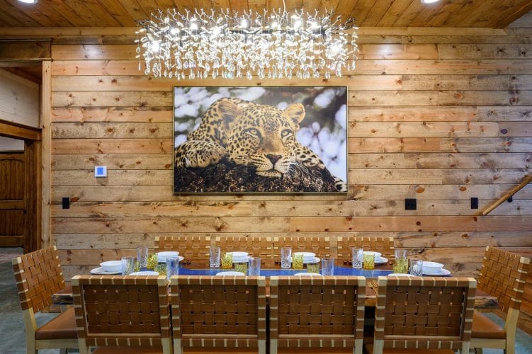 Long dining table under a chandelier with a leopard painting on the wall