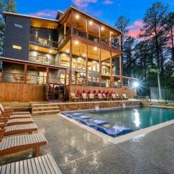 Three-story house with decks over the pool, loungers lined up along the pool edge at dusk