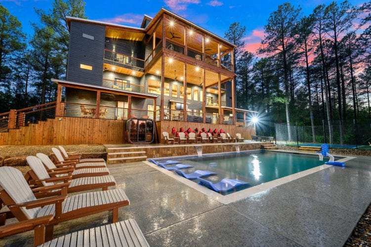 Three-story house with decks over the pool, loungers lined up along the pool edge at dusk