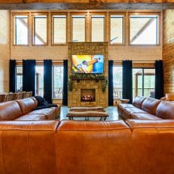 Leather sectional facing a TV above the fireplace under tall windows