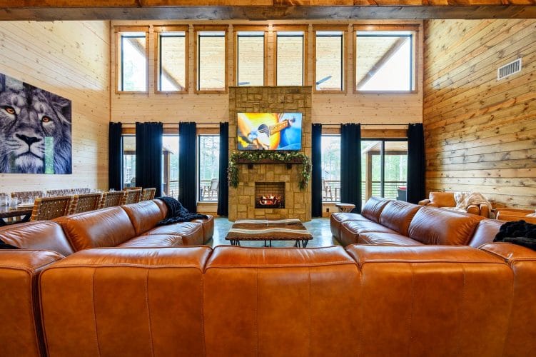 Leather sectional facing a TV above the fireplace under tall windows