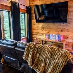 Leather couch with a throw blanket, wall TV and a shelf of colorful books