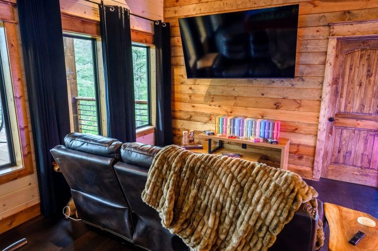 Leather couch with a throw blanket, wall TV and a shelf of colorful books