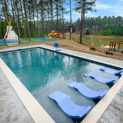 Pool with blue in-water loungers, pond and playset in the background