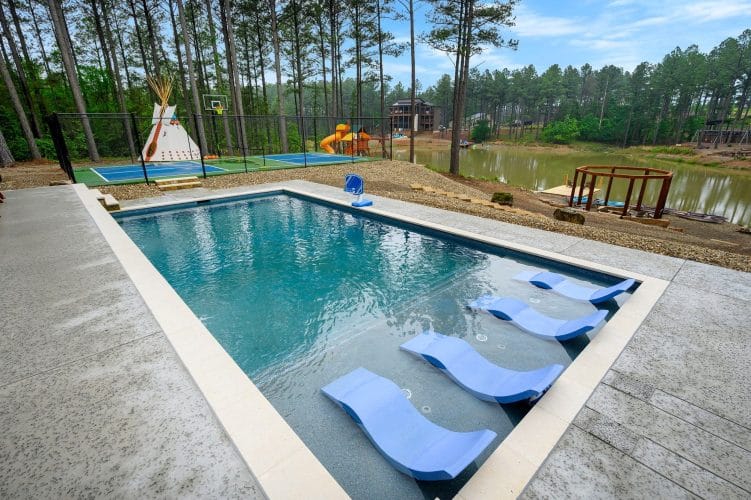 Pool with blue in-water loungers, pond and playset in the background