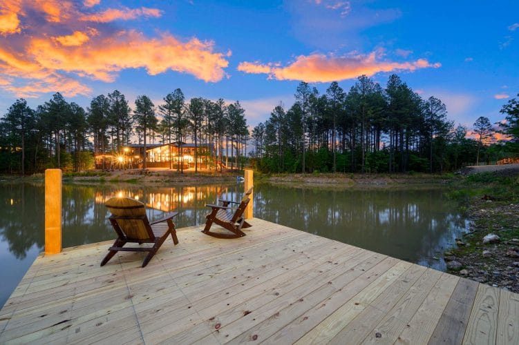 Wood dock with two Adirondack chairs on the pond at dusk