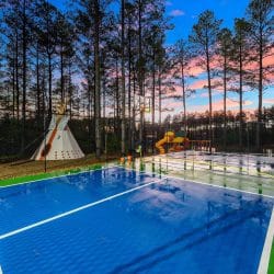 Blue pickleball court with a teepee and playset behind it