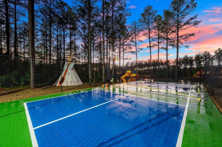 Blue pickleball court with a teepee and playset behind it