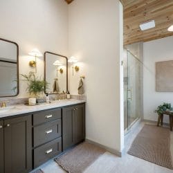 Double vanity with dark cabinets, brass fixtures, glass shower and tub in the background