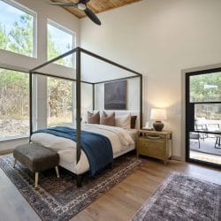 Black four-poster king bed with a blue throw and leather bench, tall windows and a glass door to the patio