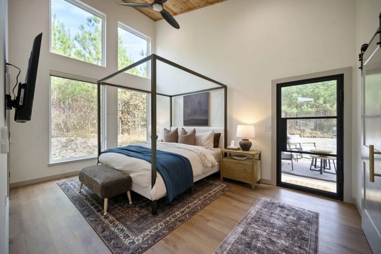 Black four-poster king bed with a blue throw and leather bench, tall windows and a glass door to the patio