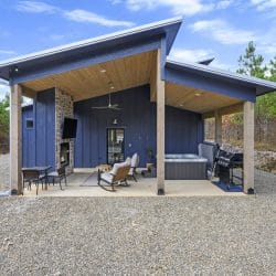 Covered patio with a stone outdoor fireplace and TV, rocking chairs, hot tub and grill