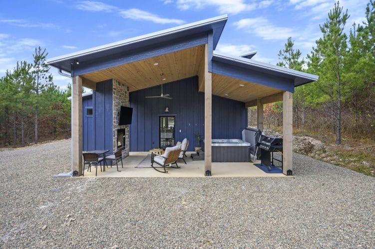 Covered patio with a stone outdoor fireplace and TV, rocking chairs, hot tub and grill