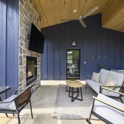 Stone fireplace and TV on the covered patio with a sofa and small tables