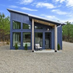 Front of the blue board-and-batten cabin with a slanted metal roof and big windows