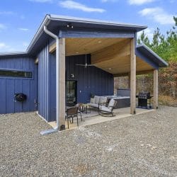 Side of the cabin with a covered patio, sofa, hot tub and grill on a gravel lot