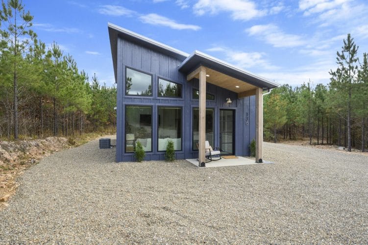 Front of the cabin with covered entry and gravel driveway under blue sky