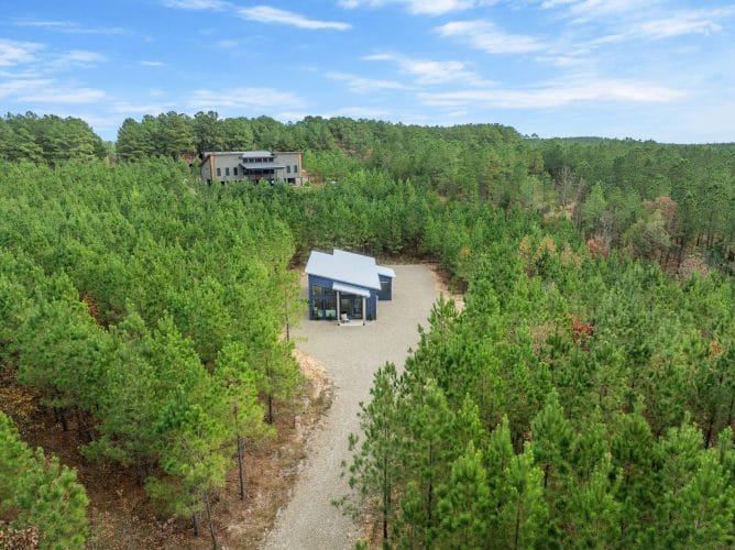 Aerial of the cabin with a larger house visible far behind it in the trees