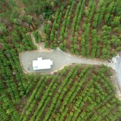 Straight-down aerial of the cabin on its gravel clearing beside the road