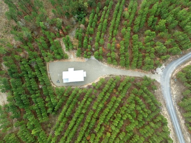 Straight-down aerial of the cabin on its gravel clearing beside the road
