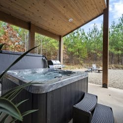 Hot tub on the covered concrete patio with the grill and gravel lot behind it